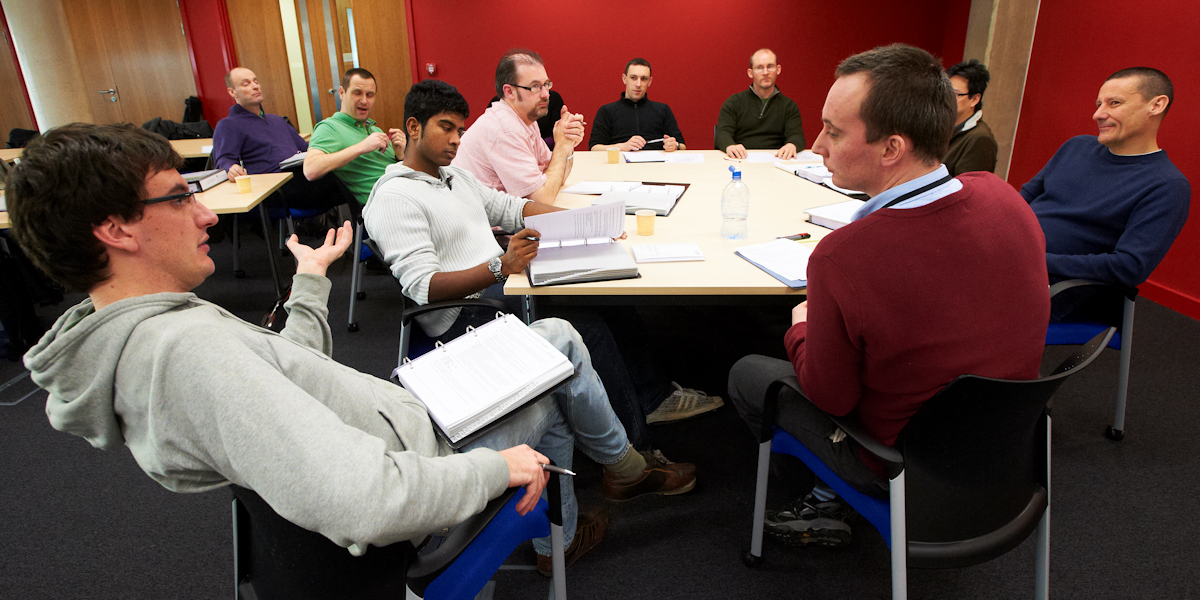 A group of students sitting around a table interacting with a lecturer